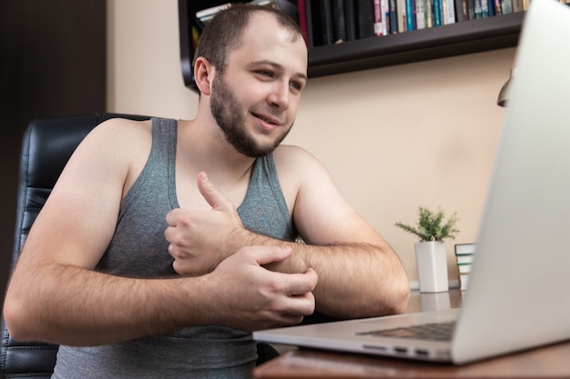  A young bearded guy in home clothes gray T-shirt, uses laptop