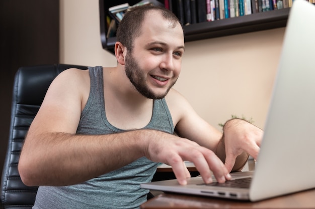 A young bearded guy in home clothes gray T-shirt, uses laptop