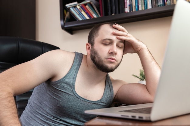 Photo a young bearded guy in home clothes gray t-shirt, uses laptop