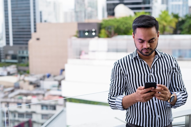 街の景色に対して若いひげを生やしたインドのビジネスマン