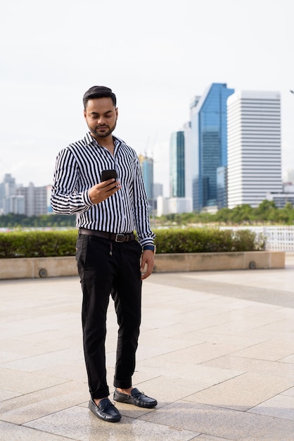 Young bearded Indian businessman relaxing at the park