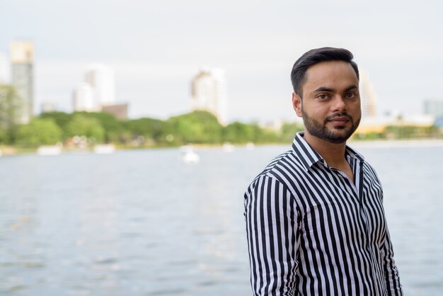 Young bearded Indian businessman relaxing at the park