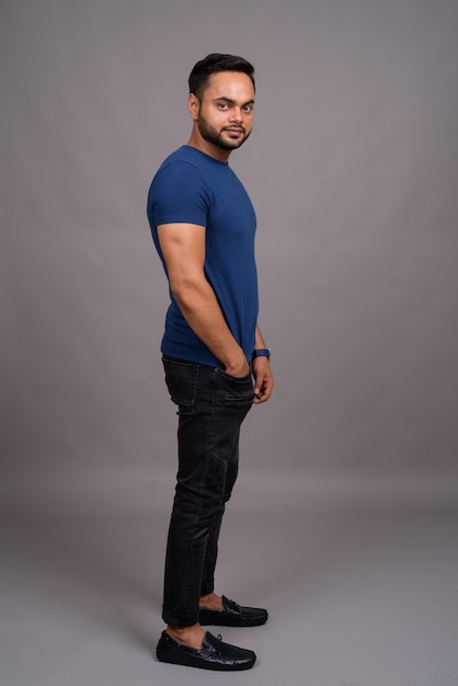 Young bearded Indian man against gray wall