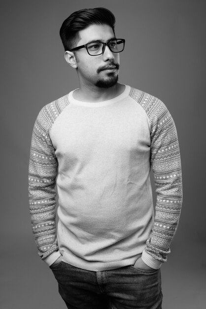  young bearded Iranian man wearing casual clothes against gray wall in black and white