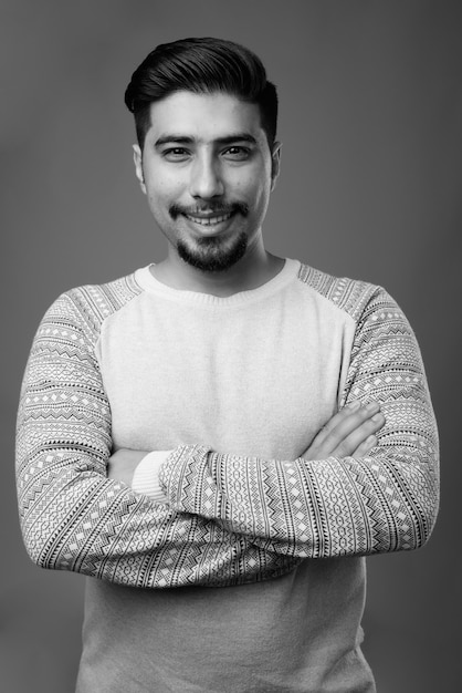  young bearded Iranian man wearing casual clothes against gray wall in black and white