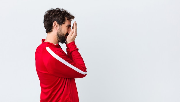 Young bearded man back view covering eyes with hands with a sad, frustrated look of despair, crying, side view against copy space wall