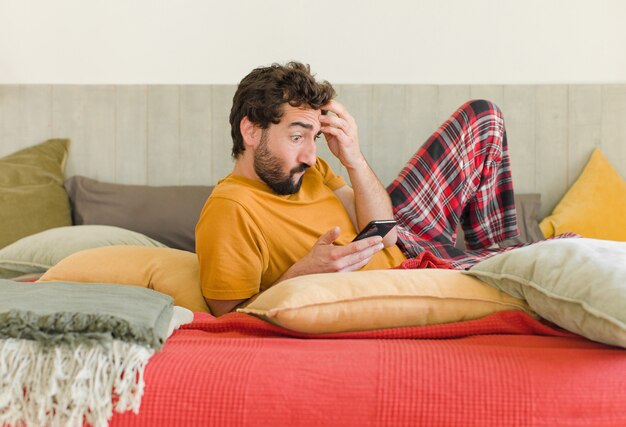 Giovane uomo barbuto su un letto con il suo telefono cellulare