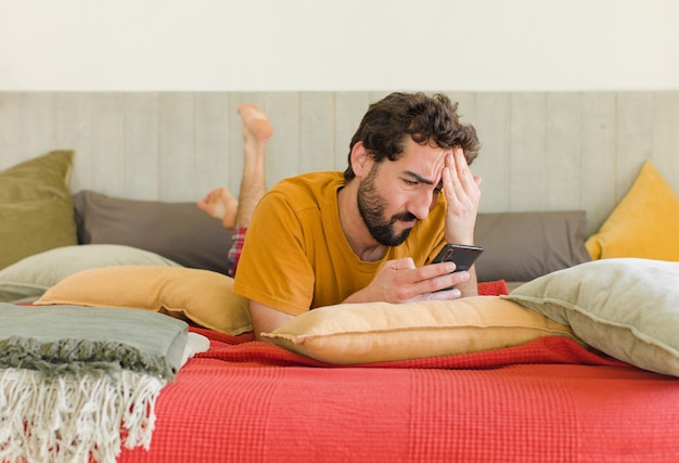 Young bearded man on a bed with his mobile phone