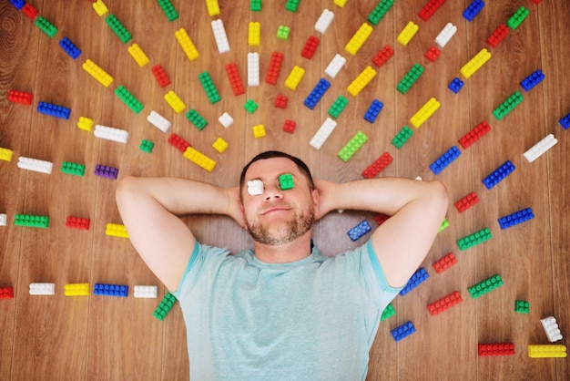 Young bearded man in a blue tshirt is smiling and grimacing lying on the floor against the backgroun