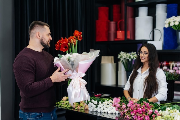 Un giovane uomo barbuto acquista un bellissimo mazzo di fiori per una vacanza di una ragazza in un accogliente negozio di fiori fiorai e bouquet in un negozio di fiori piccola impresa