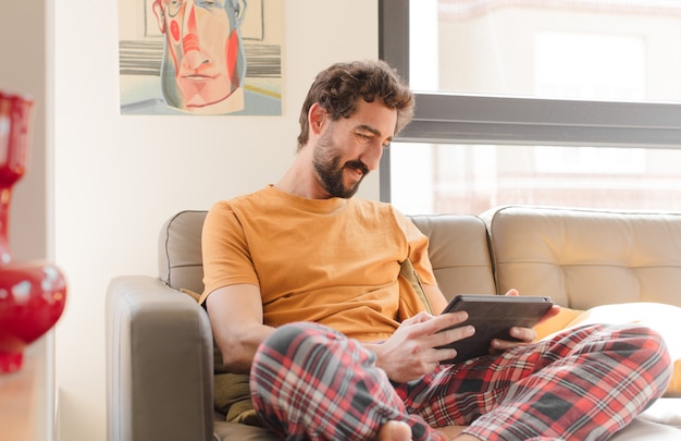 タッチスクリーンタブレットとソファの上の若いひげを生やした男