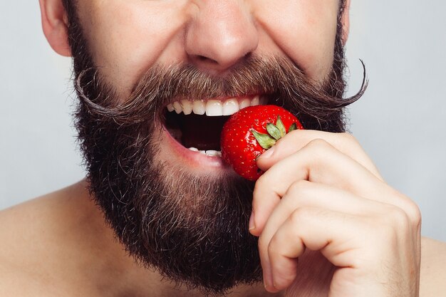 Young bearded man eating a strawberry