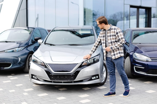 Young bearded man embracing his new car at the dealership smiling joyfully