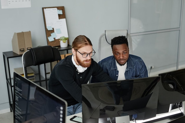 Молодой бородатый мужчина в очках и его афроамериканский коллега смотрят на экран компьютера на рабочем совещании