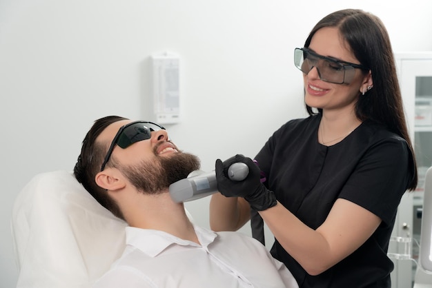 Young bearded man getting laser facial treatment by professional cosmetologist in a beauty clinic