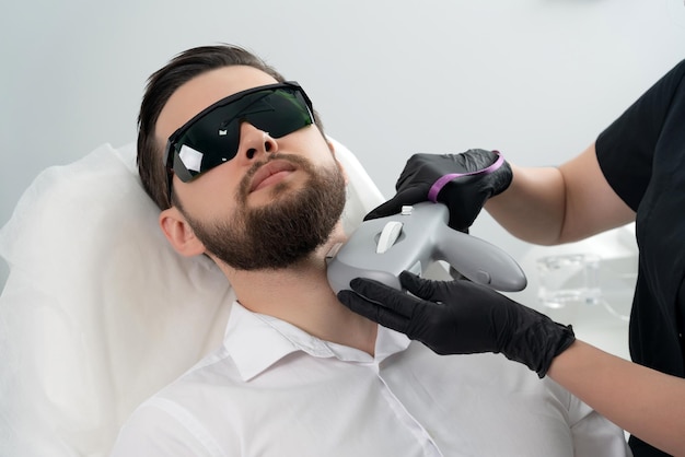 Young bearded man getting laser facial treatment by professional cosmetologist in a beauty clinic