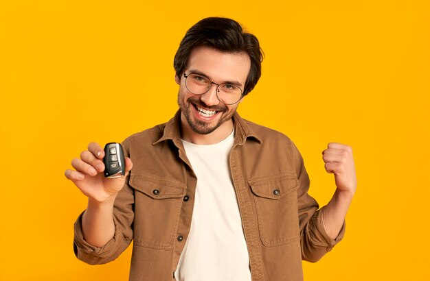 Young bearded man in glasses holds keys remote control from a new car isolated. purchase, car rental