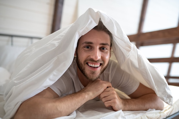 Foto giovane uomo barbuto divertendosi a letto la mattina