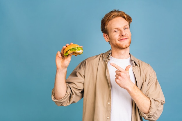 Giovane uomo barbuto che tiene un pezzo di hamburger. studente mangia fast food fast