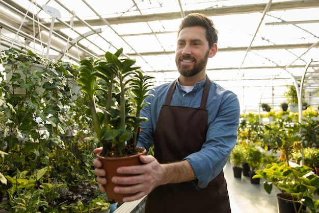 young bearded man holding a potted flower and looking contented