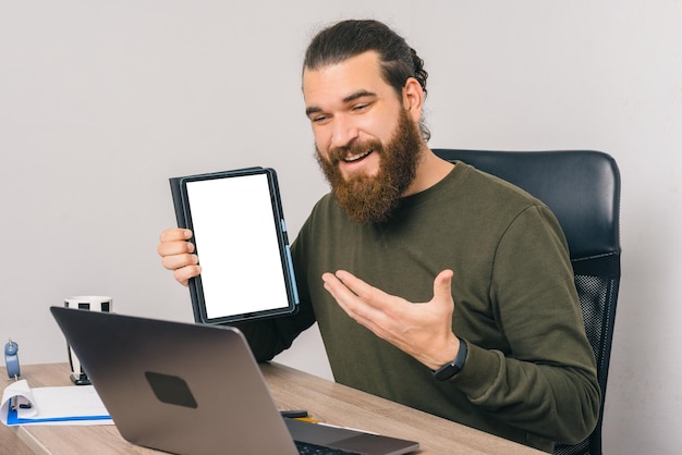 Young bearded man is explaining and showing the tablet to the video call he is having.