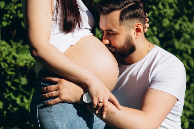 Giovane uomo barbuto che bacia la pancia della sua moglie incinta