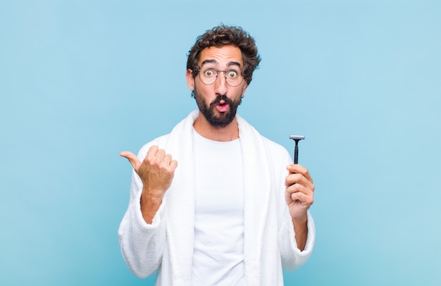 Young bearded man looking astonished in disbelief, pointing at object on the side and saying wow, unbelievable