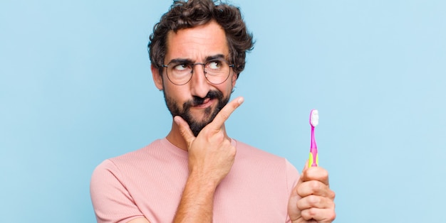 Young bearded man looking serious, thoughtful and distrustful, with one arm crossed and hand on chin, weighting options