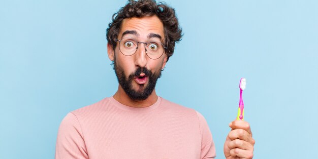 Young bearded man looking surprised and shocked, with jaw dropped holding an object with an open hand on the side