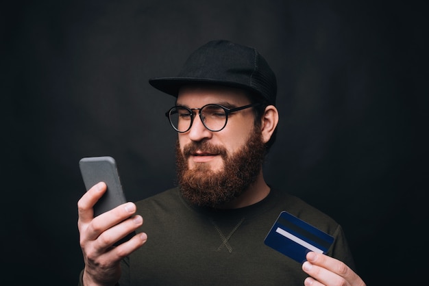 Молодой бородатый человек, сделать онлайн-заказ на свой телефон, оплата картой.