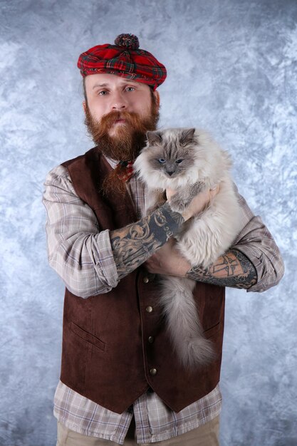 Young bearded man in plaid cap with fluffy cat on light background