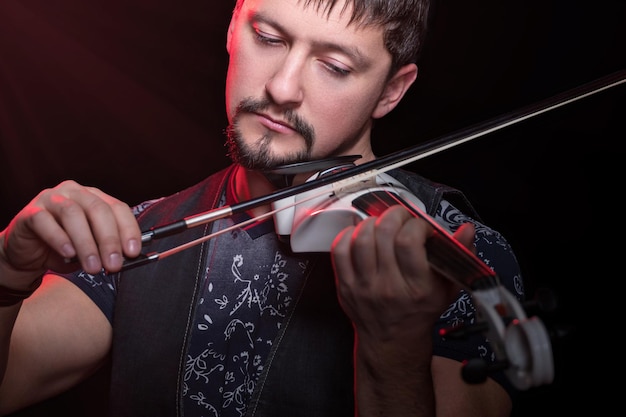 Молодой бородатый мужчина играет на белой электрической скрипке, изолированной на черном фоне
