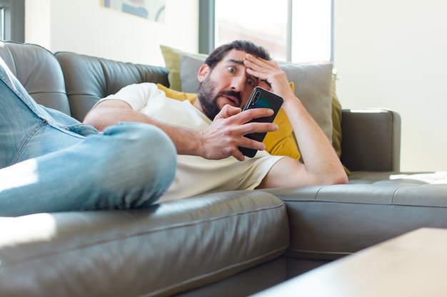 Young bearded man resting on a couch with his smartphone