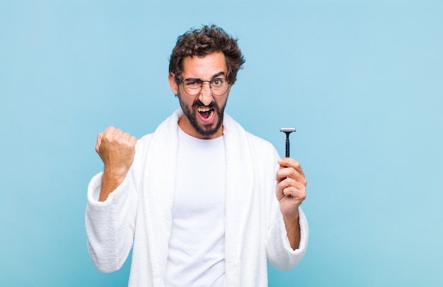 Young bearded man shouting aggressively with an angry expression or with fists clenched celebrating success