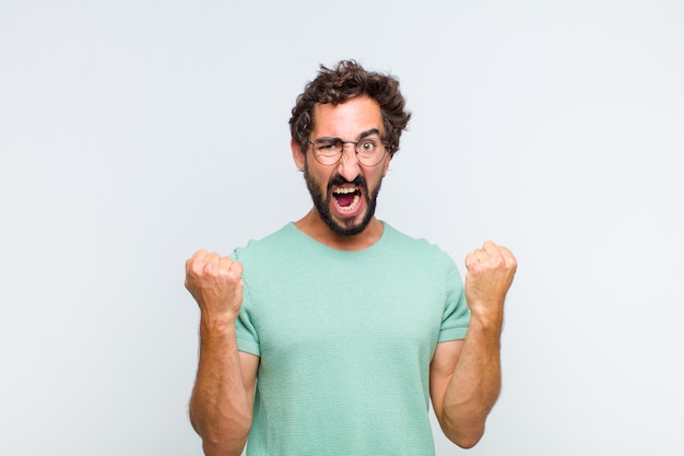 Young bearded man shouting aggressively with an angry expression or with fists clenched celebrating success