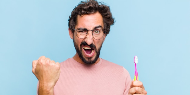 Young bearded man shouting aggressively with an angry expression or with fists clenched celebrating success