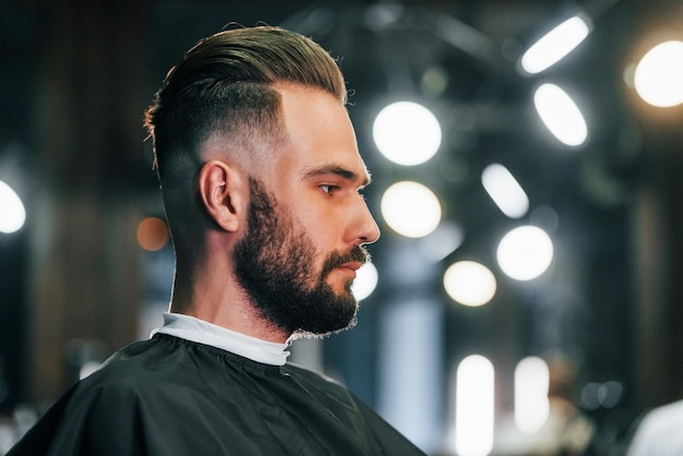 Young bearded man sitting in barber shop and waiting for stylist