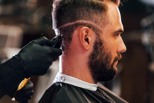 Foto giovane uomo barbuto seduto e farsi tagliare i capelli nel negozio di barbiere