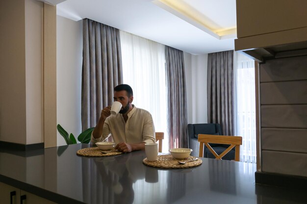 Young bearded man sitting while eating breakfast alone at home