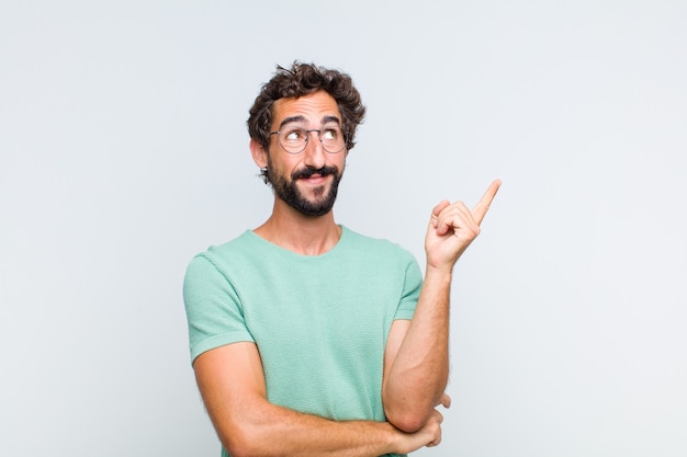 Young bearded man smiling happily and looking sideways, wondering, thinking or having an idea