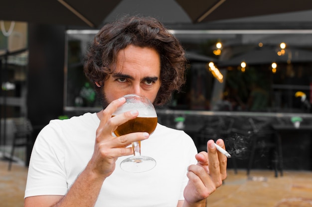 Giovane uomo barbuto che fuma e che beve una birra