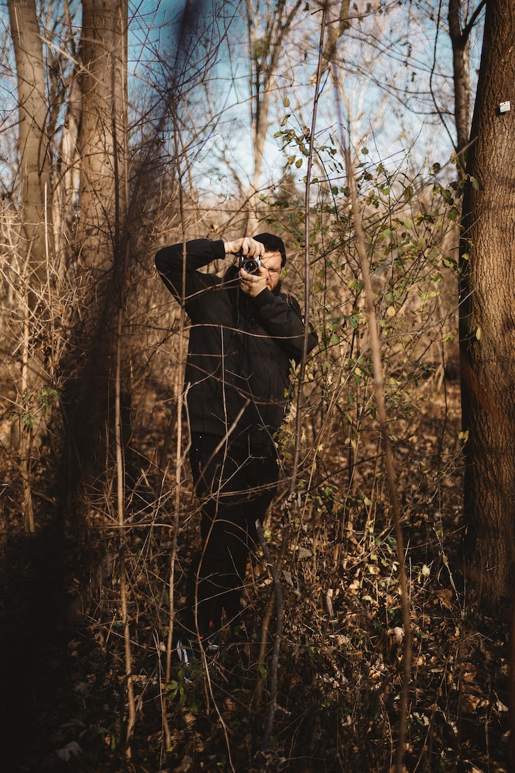 Photo a young bearded man taking a photo in the autumnal forest with a vintage photo film camera