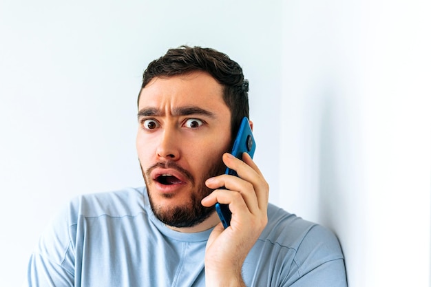 Young bearded man talking on the phone at home shocked expression of fear scared male in shock with