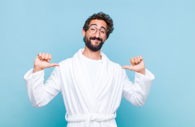 Young bearded man wearing a bath robe feeling proud, arrogant and confident, looking satisfied and successful, pointing to self