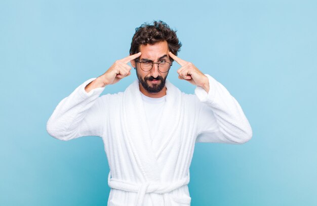 Young bearded man wearing a bath robe with a serious and concentrated look, brainstorming and thinking about a challenging problem