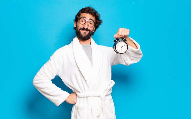 Young bearded man wearing bathrobe and an alarm clock