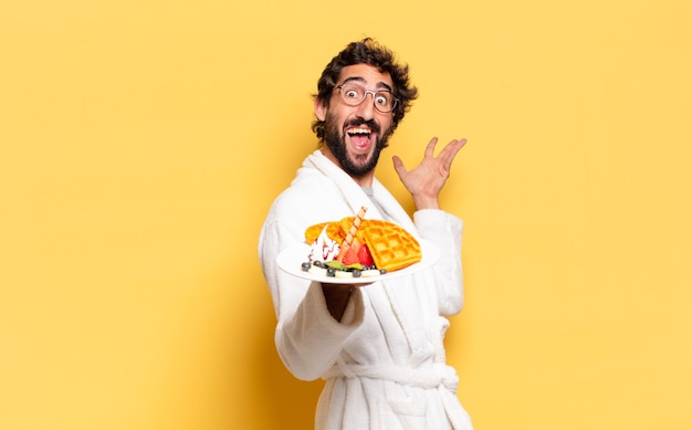 Young bearded man wearing bathrobe and having breakfast