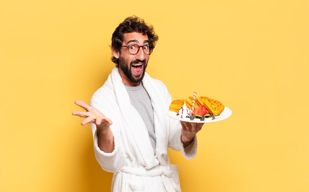 Young bearded man wearing bathrobe and having breakfast