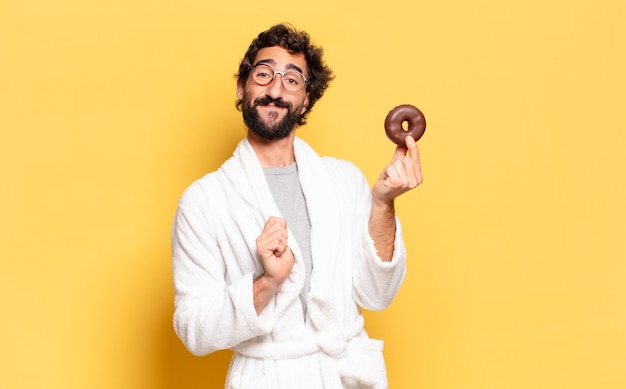 Young bearded man wearing bathrobe with a chocolate donut