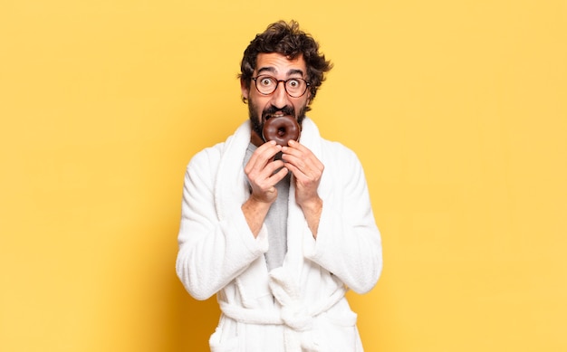 Young bearded man wearing bathrobe with a chocolate donut